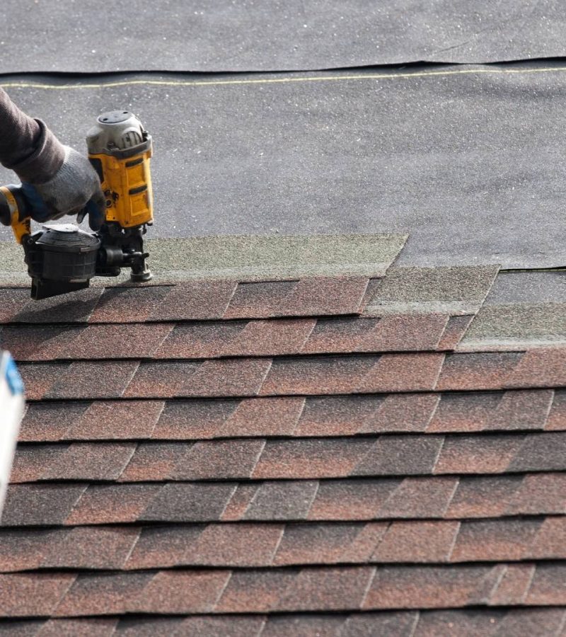professional standing on roof of home and using tool